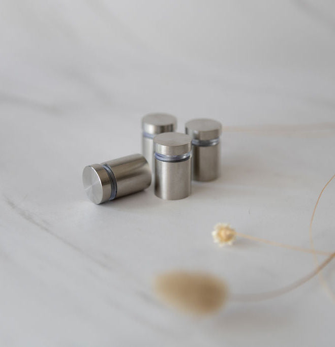 Brushed silver stainless steel standoff brackets with rubber bumpers, designed to securely mount and elevate acrylic planners off the wall for a sleek, modern floating display.